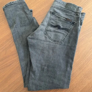 Grå jeans från Nudie Jeans - Snygga grå jeans från Nudie Jeans med klassisk femficksdesign och diskret logga på bakfickan. Jeansen har en smal passform och är tillverkade i mjukt denimtyg som ger en avslappnad vibe. Perfekta till sneakers eller boots. Modellen är Lean dean och är slimfit. Storlek 30/32 toppskick, och har fortfarande mycket kvar att ge!
