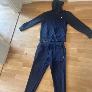 Mörkblå mjukisbyxor från Polo Ralph Lauren - Mörkblå mjukisbyxor från Polo Ralph Lauren med klassisk logga broderad på benet. Byxorna har dragsko i midjan och är tillverkade i en mjuk bomulls- och polyestermix. Perfekta för chill dagar eller när du vill vara bekväm men ändå se snygg ut.