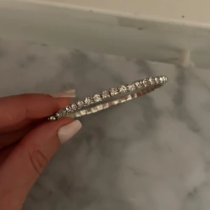 Glittrigt silverarmband med stenar - Festligt armband i silverfärg med glittrande stenar runt hela bandet. Armbandet är stelt och har en klassisk, rund form som ger en lyxig känsla.