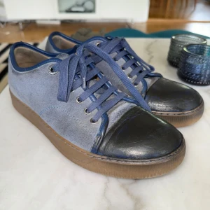 Blå sneakers från Lanvin i mocka och skinn - Snygga sneakers från Lanvin i ljusblå mocka med blå skinn-detaljer och tåparti i mörkblått skinn. Skorna har blå snörning, bruna gummisulor och rund tå. Perfekta för dig som vill ha en stilren och exklusiv look.