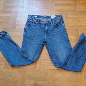 Blå jeans från Jack & Jones - Säljer ett par stilrena blå byxor från Jack n jones i storlek 14y De har en klassisk design med knappar och är perfekta för vardagar. Materialet känns slitstark och bekvämt. Passar bra till höst- och vårsäsongen. Perfekt för dig som vill ha en snygg mångsidig byxa!