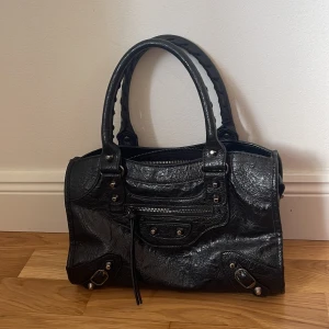 Svart handväska i skinn - (Priset kan diskuteras såklart) Cool svart handväska från Mygisova  i glansigt skinn med silverfärgade detaljer. Väskan har dubbla handtag, dragkedja upptill och en framficka med dragkedja och skinnsnören. Snygg och rymlig modell med  nitar och detaljer. Inuti finns ett stort utrymme med 2 små fickor på ena sidan och en större ficka med dragkedja på andra sidan. Nypris 600kr men säljer för 490. Kontakta vid intresse💕