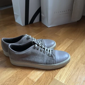Grå Lanvin sneakers i mocka och skinn - Stilrena grå sneakers med ovandel i mocka och tåparti i slätt skinn. Skorna har rund tå, snörning och vit platt sula. Perfekta för en clean och avslappnad look.