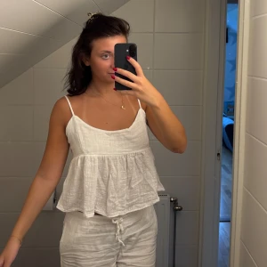 Vit linnetopp med knytning i ryggen  - Säljer en superfin vit linnetopp från Nelly som man knyter i ryggen. Toppen har tunna justerbara axelband och volang nertill. 