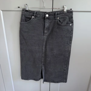 Svart jeanskjol från Carin Wester - Snygg svart (den är lite mörkare i färgen än på bilderna) jeanskjol från Carin Wester i klassisk modell med fem fickor, bälteshällor och slits framtill. Kjolen är rak och går till knäna, perfekt till sneakers eller boots. Stängs med knapp och dragkedja framtill. 