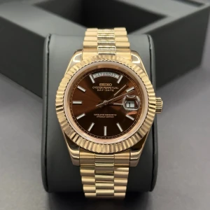 Seiko mod Day-Date president gold brown - Stilren Seiko Oyster Perpetual Day-Date med brun urtavla och dag- och datumvisning. Klockan har en klassisk rund boett i guldton och matchande länkarmband. Index och visare är i silverfärg, och glaset har förstoringsfönster vid datumet. Perfekt accessoar för dig som gillar lyxig känsla.