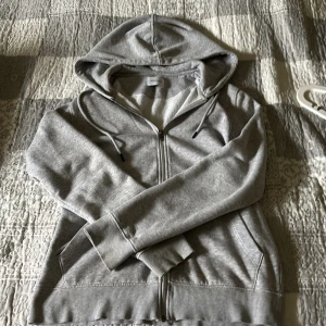 Grå hoodie med dragkedja Jack & Jones - Snygg grå hoodie från Jack & Jones i storlek XS. Tröjan har huva med snörning, dragkedja framtill och två fickor. Tillverkad i mjuk bomullsblandning, perfekt för chill dagar. Klassisk passform och ribbade muddar vid ärmslut och nederkant. Passar folk som är 170-178 och den är helt ny