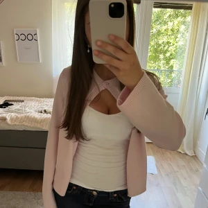 Ljusrosa kofta från Gina Tricot - Knappt använd supersöt ljusrosa kofta från Gina Tricot med rund halsringning och en knapp framtill. Koftan är stickad i mjukt material och har långa ärmar. Perfekt att slänga över ett linne för en chill och trendig look.