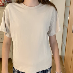 Beige t-shirt från Lindex - Enkel och stilren beige t-shirt från Lindex i storlek 170 i mjuk bomull. Modellen är rak med rund halsringning och korta ärmar, perfekt för en clean och avslappnad look. Passar dig som gillar basic och neutrala färger. Använd många gånger men fortfarande ett mycket bra skick.