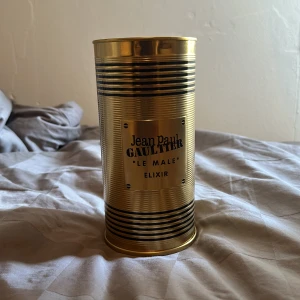 Jean Paul Gaultier Le Male Elixir 125ml - Jean Paul Gaultier Le Male Elixir EdP i en ikonisk guld- och svart randig metallburk. Flaskan är formad som en manlig torso i guld med svarta ränder och står på en röd sammetsliknande bas. Volymen är 125 ml. En lyxig och unik parfymflaska som sticker ut i samlingen.
