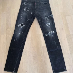 Dsquared2 jeans äkta  - Säljer ett par svarta jeans med coola slitningar och hål på både fram- och baksida. Jeansen har raka ben och klassisk femficksmodell. Perfekta för dig som gillar en edgy streetstil.