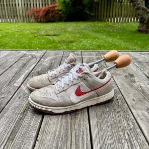 Nike Dunk Low i beige och rött mocka - Säljer mina riktigt feta dunks. Skorna är väldigt unika och passar perfekt för dig som vill sticka ut! På bilden är skorna lite smutsiga vilket går att fräscha upp, skorna har även en lite slitage defekt som syns på bilderna. Strl är 38,5. Hör av er vid frågor!