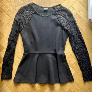 Svart peplumtop med spetsärmar Gina Tricot - Supersnygg svart peplumtop från Gina Tricot med långa ärmar i blommig spets. Toppen har rund halsringning och markerad midja som ger en feminin siluett. Perfekt för dig som gillar detaljer och vill sticka ut lite extra.