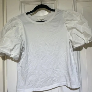 Vit puffärm topp från H&M XS - Vit topp från H&M i storlek XS med trendiga puffärmar och rund halsringning. Tillverkad i mjuk bomull som känns skön mot huden. Enkel och stilren design som passar perfekt till jeans eller kjol för en fräsch look.