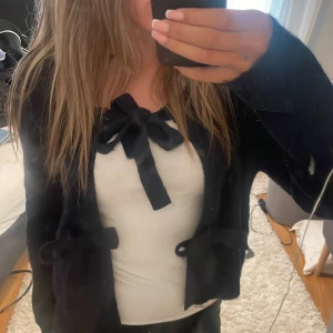 Mörkblå  kofta med rosetter - Säljer en mörkblå kofta med långa ärmar och tre söta rosetter framtill. Koftan är croppad och har en mjuk, stickad känsla som passar perfekt till lager-på-lager. Enkel att matcha med olika outfits för en trendig look.