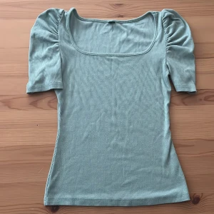 Ljusgrön ribbad topp med puffärm - Superfin ljusgrön topp med fyrkantig ringning och korta puffärmar. Toppen är ribbad och har en slim passform som sitter snyggt på kroppen. Perfekt att styla med jeans eller kjol för en fräsch look.