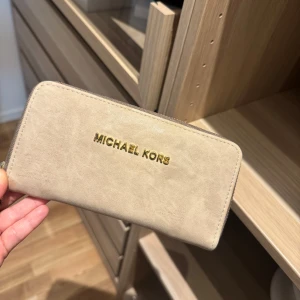 Beige plånbok från ”Michael Kors” - Snygg beige plånbok i mjukt skinn med guldfärgad logga framtill. 