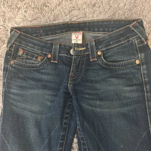 True Religion bootcut jeans  - Snygga blå jeans från True Religion med klassiska kontrastsömmar och ikonisk broderad ficka bak. Bootcut-modell med låg midja och råa, fransiga benslut. Tillverkade i stretchig denim för skön passform. Perfekta för dig som gillar en avslappnad men trendig look, dom är sydda till bootcut och ser faktiskt ut som de men har ingen bra bild, kan skicka bättre bilder. (Pris kan jättegärna diskuteras)