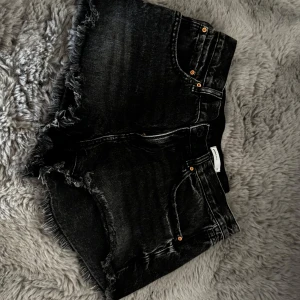 Svarta jeansshorts  - Snygga svarta jeansshorts från gina tricot med råa, fransiga kanter och klassisk femficksdesign. Shortsen har dragkedja och knapp framtill samt slitna detaljer för en cool vibe. Perfekta för sommardagar och festivaler.