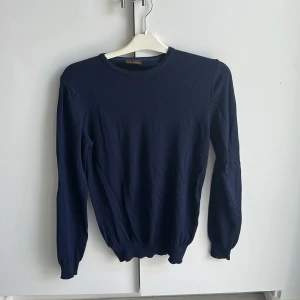 Mörkblå stickad tröja från Stenströms - En klassisk mörkblå stickad tröja från Stenströms med rund halsringning och långa ärmar. Tröjan har ribbade muddar vid ärmslut och nederkant, vilket ger en snygg och enkel look. Perfekt för lager-på-lager och stilrena outfits.