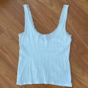 Vit linnetopp med spetskant - Vit linnetopp med ribbat mönster och spetsdetaljer längs urringningen och axelbanden.