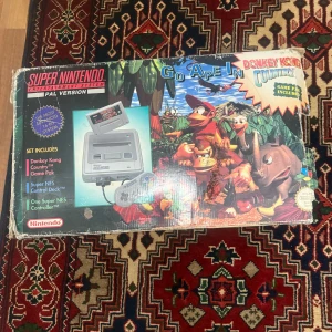 Super Nintendo Entertainment System - Klassisk Super Nintendo Perfekt för retrospelare och samlare. Innehåller konsol, handkontroll och spelet Donkey Kong Country. Låt nostalgin flöda och utmana dina vänner i denna ikoniska plattformsklassiker. Ingår med en spel
