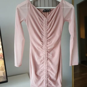 Rosa omlottklänning PrettyLittleThing - Supersöt ljusrosa kortklänning från PrettyLittleThing med långa ärmar och snygg rynkdetalj framtill. Klänningen har v-ringning och är gjord i ett tunt, lätt material som känns bekvämt. 