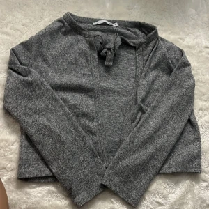 Grå omlottkofta från 157, M - Mysig grå kofta från 157 i omlottmodell med knyt framtill. Tröjan är långärmad och har en croppad passform som ger en chill vibe. Materialet är mjukt och stickat, perfekt för lager på lager under höst och vinter.