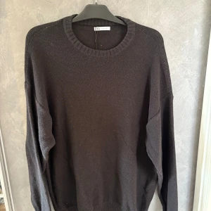 Svart stickad tröja från Zara Man - En svart stickad tröja från Zara Man med rund halsringning och ribbade muddar. Tröjan har en enkel och clean design med lång ärm och relaxed fit, perfekt för lager-på-lager under kyliga dagar.