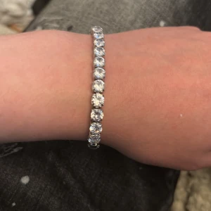 Silverfärgat tennisarmband med stenar - Snyggt tennisarmband i silverfärg med gnistrande runda stenar längs hela bandet. Perfekt för dig som gillar klassisk och stilren design med extra bling. Lätt att matcha med andra smycken och ger en lyxig känsla till din outfit.