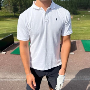 Vit pikétröja från Ralph Lauren - Vit pikétröja från Ralph Lauren med korta ärmar och krage. Broderad logga på bröstet. Tillverkad i mjuk bomull som känns skön mot huden. Perfekt för en clean och stilren look. 