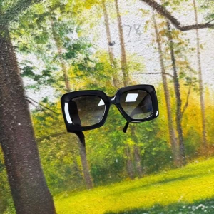 Svarta fyrkantiga solglasögon Chane - Snygga svarta solglasögon från Chane med breda skalmar och fyrkantig oversized form. Sidorna har gulddetaljer och små glittriga stenar vid gångjärnen samt den ikoniska Chanel-loggan. Perfekt accessoar för att lyfta din stil.