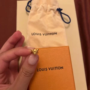 Louis Vuitton guld V-örhänge - Snyggt örhänge från Louis Vuitton i form av ett stilrent V. Örhänget är i guldfärgad metall och har en minimalistisk design som känns både lyxig och modern. Kommer med originalpåse, ask och kvitto. Perfekt accessoar för dig som gillar exklusiva detaljer.Tappat bort ena så det är endast ett örhänge som säljes!