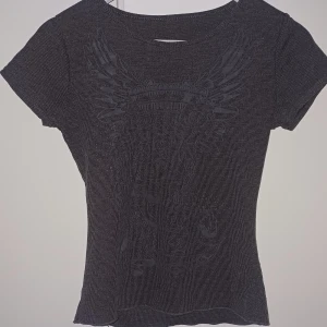 Mörk grå tröja med tryck  - Cool ribbad topp med korta ärmar och ett diskret tryck framtill som föreställer vingar och blommor. Tight passform ‼️man kan inte se trycket så bra om du kollar på sista bilden 🥲‼️ 