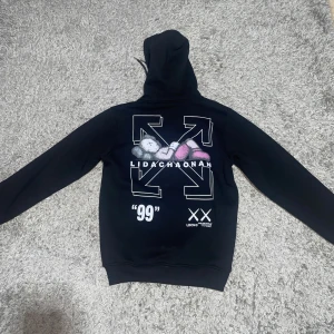 Svart Off-White hoodie med tryck - Svart hoodie från Off-White med vit text och XX-tryck framtill. Baksidan har stort grafiskt tryck med pilar, text och motiv i vitt, grått och rosa. Klassisk känguruficka, huva med snörning och ribbade muddar. Perfekt statement-plagg för streetwear-stilen. Helt ny och aldrig använd.