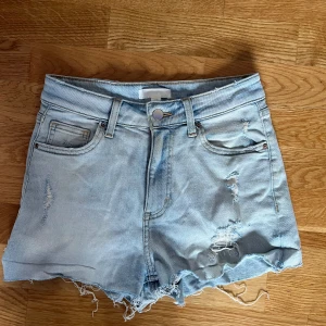 Ljusblå jeansshorts från H&M - Snygga ljusblå jeansshorts från H&M i klassisk femficksmodell. Shortsen har slitna detaljer, fransig nederkant och normal passform. Perfekta för sommaren och ger en avslappnad vibe till din outfit. 