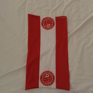 Rödvit Degerfors halsduk - Snygg halsduk i rött och vitt med breda ränder och Vulkanerna Supporterklubbs logga tryckt i båda ändar. Perfekt accessoar för att visa ditt stöd på matchen eller när du vill representera laget.