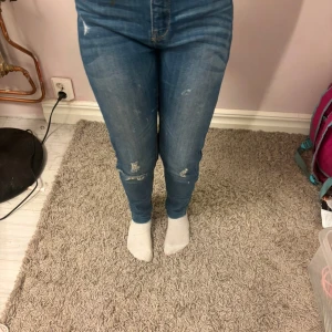 Blå skinny jeans med slitningar - Säljer ett par blå skinny jeans med snygga slitningar på knäna . Jeansen har en femficksdesign, (mid waist) längden på jeansen är 140-155.