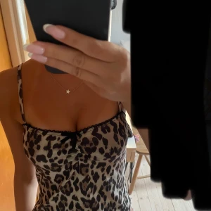 Leopardmönstrad topp från Gina tricot - Säljer en snygg kort klänning med leopardmönster och tunna axelband. Klänningen har en liten svart rosett framtill och svarta spetsdetaljer längs urringningen. Perfekt för dig som vill sticka ut med en trendig look.