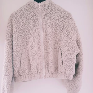 Beige teddyjacka med dragkedja strl M - Supermjuk och fluffig beige teddyjacka med hel dragkedja framtill och två fickor. Jackan har hög krage och är perfekt för kyliga dagar. Oversized känsla och riktigt cozy look som passar till allt. Materialet är teddy/fleece och jackan är långärmad.  Helt skick dock "urtvättade" muddar