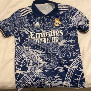 Fotbolls tröja - Säljer en blå Real Madrid fotbollströja från Adidas i storlek S. Tröjan har ett fett drakmönster i vitt över hela plagget, klassisk krage och korta ärmar. Officiella klubbmärket och Adidas-logga på bröstet. Materialet är lätt och andas, perfekt för match eller träning. Använt den fåtal gånger den e tvättad såklart, skit snygg. Pris går att diskutera. Frågor dm bara.