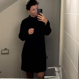 Stickad klänning  - Mysig svart stickad klänning med lång ärm och hög hals. Tjockt stickat material som är både snyggt och bekvämt. Jättefin att styla med vad som helst, både lätt att klä upp och lätt att klä ner. 