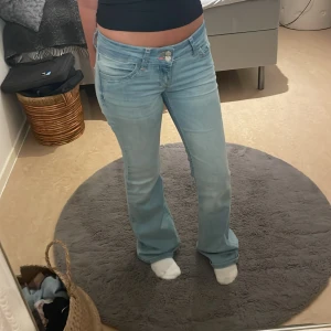 Ljusblå bootcut jeans från Nelly - Säljer ett par ljusblå jeans från Nelly med bootcut passform och låg midja. Jeansen har dubbla knappar framtill, klassiska fickor och snygga broderade detaljer på bak fickorna. De är stretchiga och är i storlek Xs💕