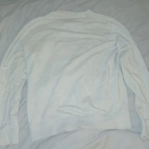 Ljusgrå sweatshirt från Lyle & Scott - En stilren ljusgrå sweatshirt från Lyle & Scott med klassisk rund hals och broderad gul logga på bröstet. Tröjan har långa ärmar och är tillverkad i mjuk bomull, och den har aldrig blivit använd och Swratshirten har bara ligit i min garderob.