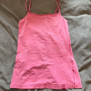 Rosa linne med broderi - Säljer ett rosa linne med smala axelband och broderad logga framtill. ❤️Linnet är mjukt och har en enkel, clean look som passar perfekt till jeans eller kjol!😍Storlek M men passar även mig med s!❤️