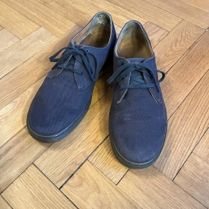 Dr. Martens Delray blå sneakers - Snygga Dr. Martens Delray i marinblå canvas med marinblå snören och robust gummisula. Klassisk rund tå och låg profil, perfekt för dig som gillar stilrena och bekväma sneakers med en twist. Storlek 42 EU. Dom är inte särskilt mycket använda som man kan se på sulan. Dock har mina hälar en tendens att slita upp innerfodret som syns på sista bilden. Båda skorna är slitna på samma sätt. 
