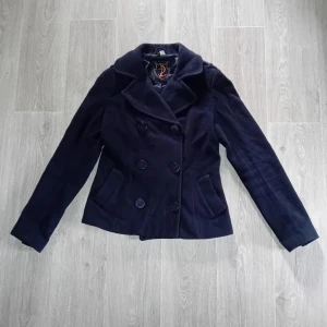 Mörkblå kappa med knappar - Säljer en snygg mörkblå jacka/kappamed dubbelknäppning och stora knappar. Jackan har en klassisk stil med långa ärmar och är perfekt för höst. 