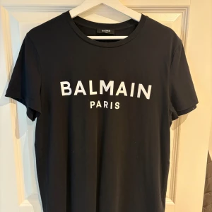 Svart Balmain Paris t-shirt i bomull - Snygg svart t-shirt från Balmain Paris med vit logga framtill. T-shirten är knappt använd och är som ny! (Nypris 3300 Miinto)