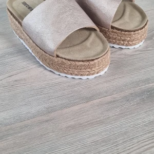 Platåsandaler Walking on Clouds 38 - Snygga platåsandaler i ljusrosa metallic med bred rem i skinn och mjuk innersula. Sulan är flätad i jute-look och har en vit räfflad undersida för extra grepp. Perfekta för sommaren och ger en trendig touch till din outfit.