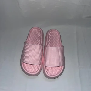 Ljusrosa sandaler med ribbad rem - Säljer ett par ljusrosa sandaler med bred ribbad rem och mönstrad sula för extra komfort. De är tillverkade i syntetmaterial och har öppen tå och platt sula. Perfekta för sommardagar eller att chilla hemma.